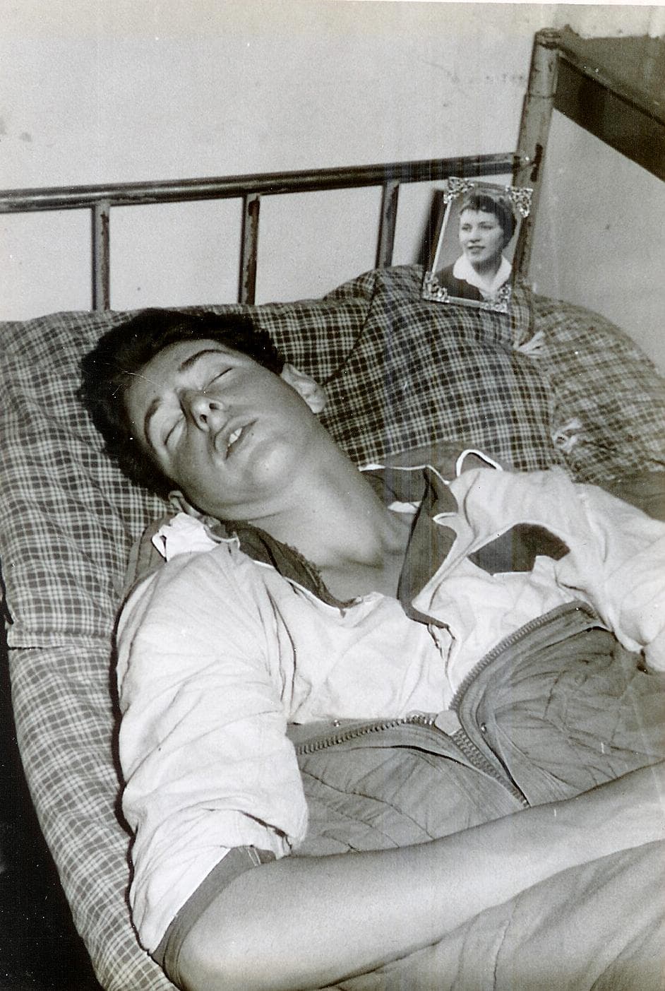 Een jonge soldaat slaapt op een ijzeren bed, met een fotootje van zijn vriendin naast het kussen